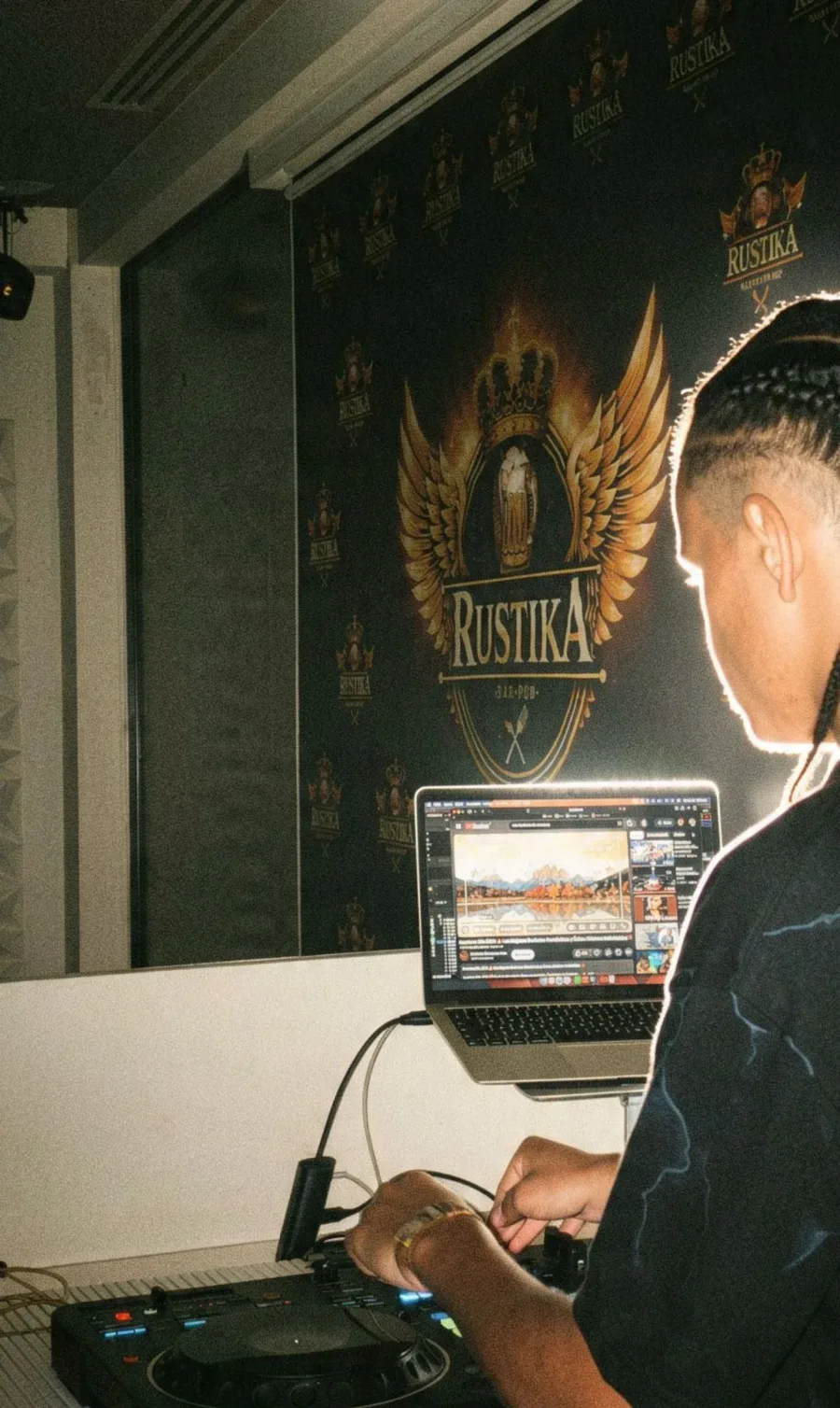 Il DJ set al Rustika Il DJ alla consolle davanti al backdrop con il logo Rustika Bar Pub